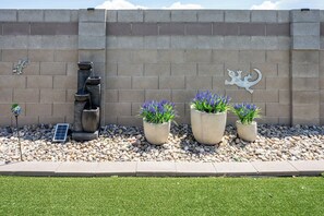Un espace paysager agrémenté d’un élément aquatique, de plantes en pot et d’œuvres d’art décoratives murales.