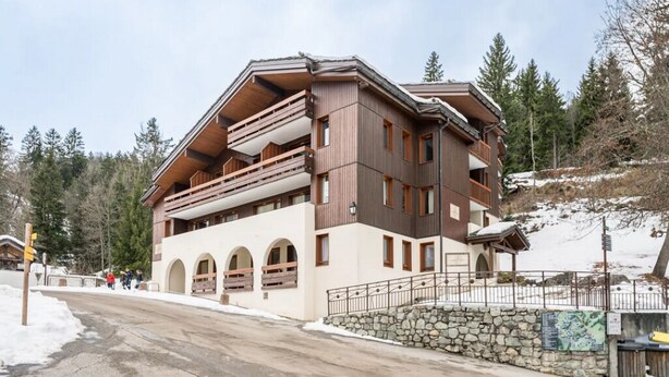 A multi-story building with balconies, a stone wall, and a snowy landscape. - Apartment, les Avanchers Valmorel, sleeps 6. (Les Avanchers-Valmorel)