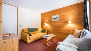 A compact living space with a yellow sofa, a wooden coffee table, and a bed with a grey cover. - Apartment, les Avanchers Valmorel, sleeps 6. (Les Avanchers-Valmorel)