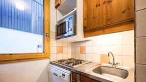 A compact kitchen with a built-in microwave, a stove, and a sink. - Apartment, les Avanchers Valmorel, sleeps 6. (Les Avanchers-Valmorel)