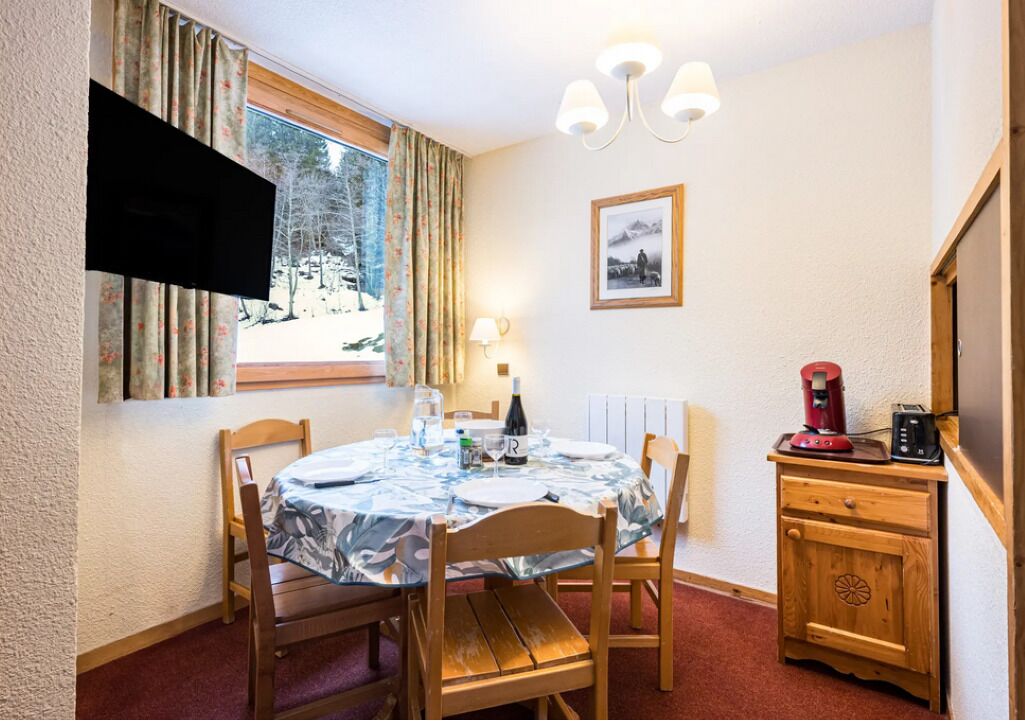 Un coin repas accueillant avec une table ronde, des chaises, un téléviseur fixé au mur, une machine à café et un tableau encadré.