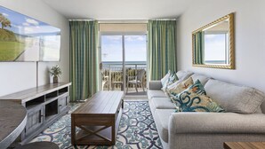 Een woonkamer met een bank, salontafel, televisie en een balkon met uitzicht op zee.