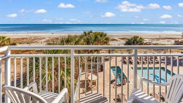 Een balkon met witte stoelen, een zwembad en uitzicht op het strand en de oceaan.