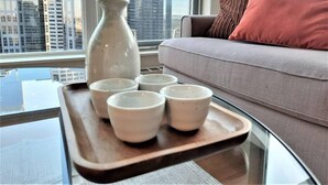 A modern living room with a glass coffee table, a grey sofa, and a city view through large windows. - Luxury Condo by River w/City Views (Calgary)