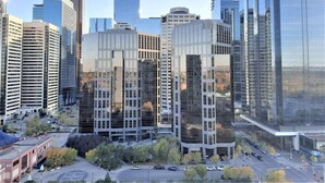 A modern urban area with high-rise buildings, including a distinctive building with a unique facade and a large glass structure. - Luxury Condo by River w/City Views (Calgary)