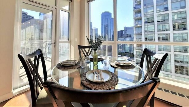 A dining area with a round glass table, black chairs, and a city view through large windows. - Luxury Condo by River w/City Views (Calgary)