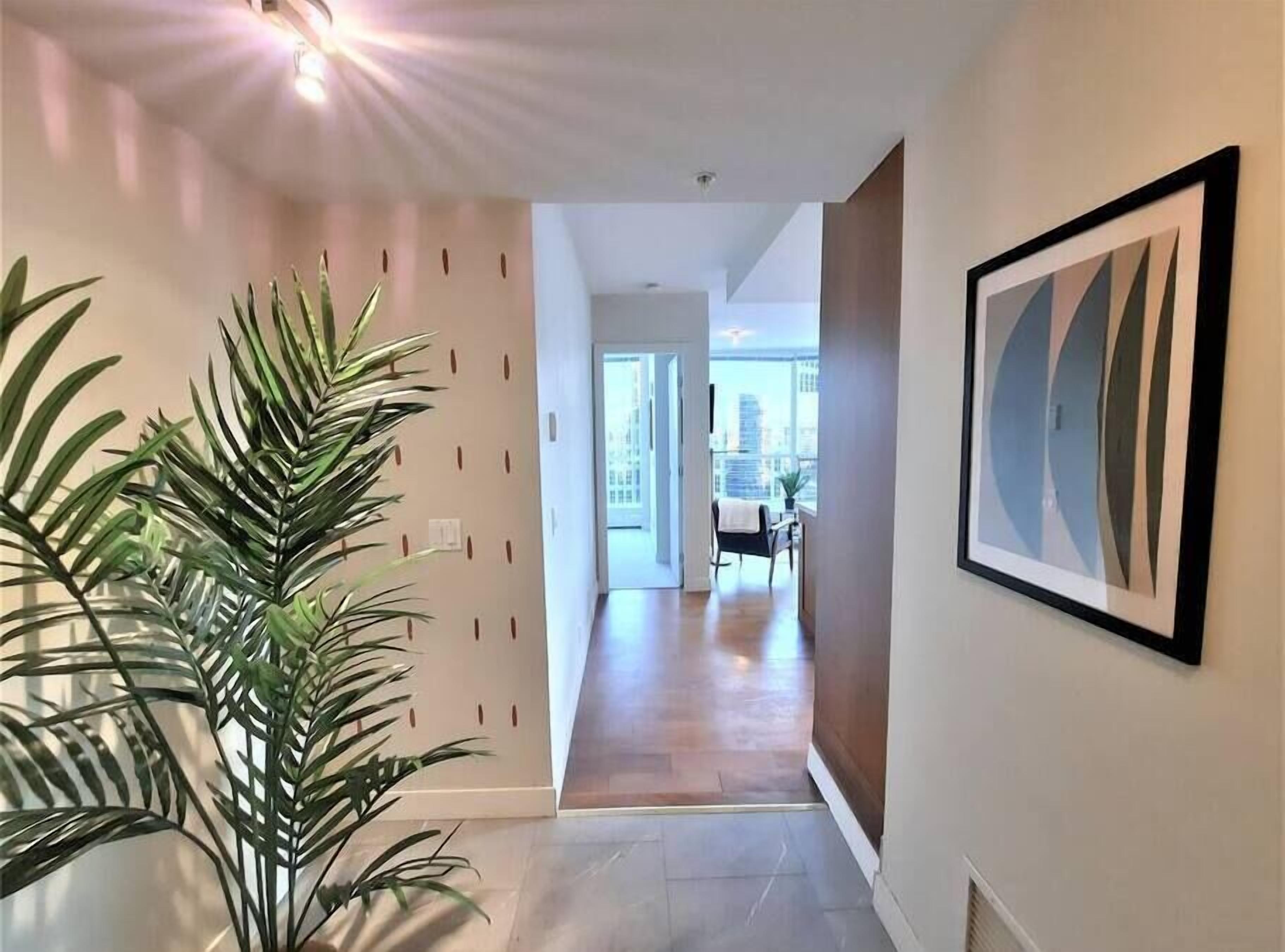 A hallway with a potted plant, a framed abstract artwork, and a view of a dining area with a chair and table.