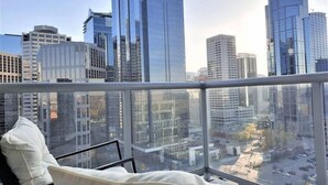 A high-rise hotel room with a city view, a bed, and a window with a view of the urban skyline. - Luxury Condo by River w/City Views (Calgary)