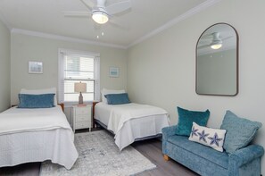 Une chambre avec deux lits, une table de chevet, une commode, un miroir et un canapé bleu agrémenté de coussins décoratifs.