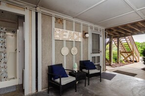 A covered outdoor seating area with two wicker chairs, a 'BEACH' sign, and a wooden staircase leading to a deck.