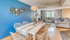 Un salon moderne avec un coin repas, agrémenté d’un mur d’accent bleu, de meubles en osier et d’un luminaire suspendu.