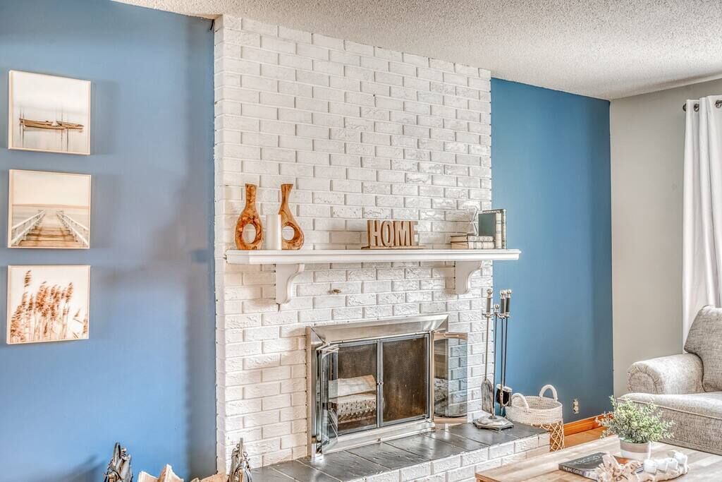 Un salon avec une cheminée en briques blanches, un mur d’accent bleu et un canapé.