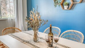Une table à manger avec une bouteille de vin, deux verres et un vase de fleurs séchées.