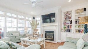 A spacious living room with a fireplace, a television mounted above it, and a bookshelf filled with books and decorative items. - 3 Bedroom Lower Duplex w Ocean Views and Game Room (Wrightsville Beach)