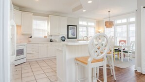 A modern kitchen with white cabinetry, a central island, and a dining area with white chairs. - 3 Bedroom Lower Duplex w Ocean Views and Game Room (Wrightsville Beach)