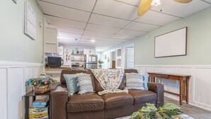 Ein Wohnzimmer mit einem braunen Ledersofa, einem Couchtisch mit einer Pflanze und einer Küche im Hintergrund.