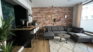 Ein moderner Wohnraum mit einer Küche, einem grauen Ecksofa, einem kleinen Couchtisch und einer Ziegelwand.