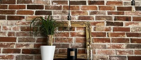 A brick wall with a white potted plant and a black candle on a wooden shelf.