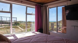 A bedroom with a large bed, two windows, and a view of the outdoors. - Beautiful House, Wave/Surf Steps. Point of Wolves (pichilemu)