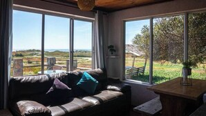 A room with a leather sofa, a small table, and large windows offering a view of a landscape. - Beautiful House, Wave/Surf Steps. Point of Wolves (pichilemu)