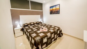 A bedroom with a large bed, a nightstand, a bedside table, and a cityscape painting on the wall.