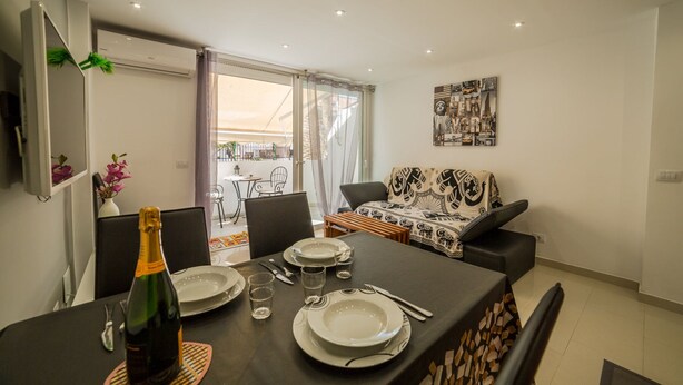 A dining area with a table set for two, a sofa, and a balcony with a view.