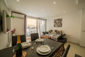A dining area with a table set for two, a sofa, and a balcony with a view.