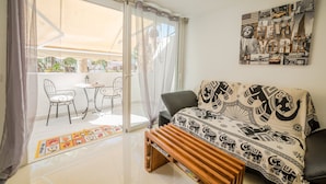 A living room with a sofa, a wooden bench, a table with chairs, and a large window with sheer curtains.