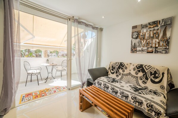 A living room with a sofa, a wooden bench, a table with chairs, and a large window with sheer curtains.