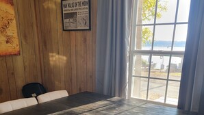 A conference room with a large table, chairs, a wooden wall, a framed picture, and a window with a view.