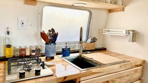 Een kleine keuken met een spoelbak, een houten aanrechtblad en een raam boven de spoelbak.