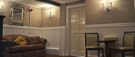A hotel room with a patterned sofa, a dining table with chairs, a mirror, and a door labeled "The Bankey Suite."