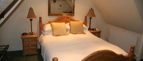 Una cama bien hecha con cabecera de madera, dos mesitas de noche con lámparas, un espejo sobre la cama y un radiador en la pared.