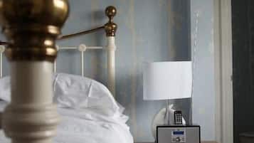 Een net opgemaakt bed met witte lakens, een nachtkastje met een lamp en een bijzettafeltje met een afstandsbediening.
