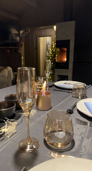 Een eettafel gedekt met wijnglazen, een kaars en een kerstboom op de achtergrond.