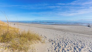 A wide sandy beach with gentle waves, clear skies, and distant horizon. - Lavish Accessible On Ocean: 4 Kings, Huge Private Pool/Yard/Spa/Patio/GameTables (North Myrtle Beach)