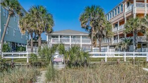 A beachfront hotel with a white fence, palm trees, and a clear sky. - Lavish Accessible On Ocean: 4 Kings, Huge Private Pool/Yard/Spa/Patio/GameTables (North Myrtle Beach)