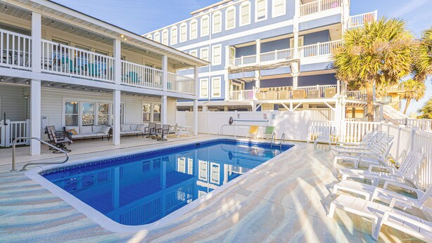 A pool area with lounge chairs, a pool, and a multi-story building with balconies. - Lavish Accessible On Ocean: 4 Kings, Huge Private Pool/Yard/Spa/Patio/GameTables (North Myrtle Beach)