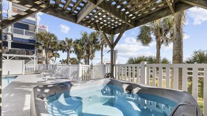 A hot tub area with lounge chairs, a pool, and a view of palm trees and a building. - Lavish Accessible On Ocean: 4 Kings, Huge Private Pool/Yard/Spa/Patio/GameTables (North Myrtle Beach)