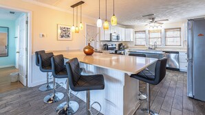 A modern kitchen with a central island, bar stools, pendant lighting, and stainless steel appliances. - Lavish Accessible On Ocean: 4 Kings, Huge Private Pool/Yard/Spa/Patio/GameTables (North Myrtle Beach)