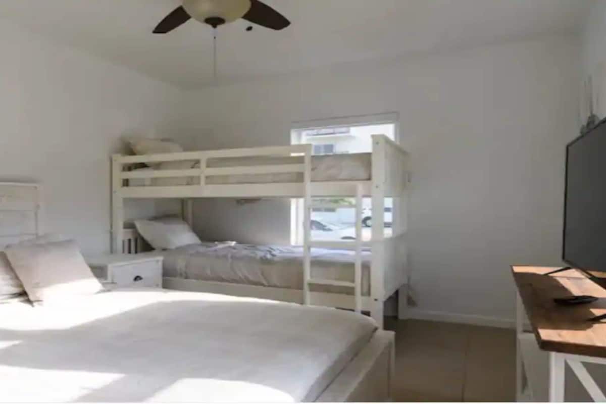 Une chambre avec un lit superposé, un lit simple, un bureau avec une télévision et un ventilateur de plafond.