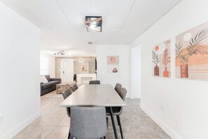 Un comedor moderno con una mesa larga y sillas, una cocina al fondo y obras de arte en las paredes.