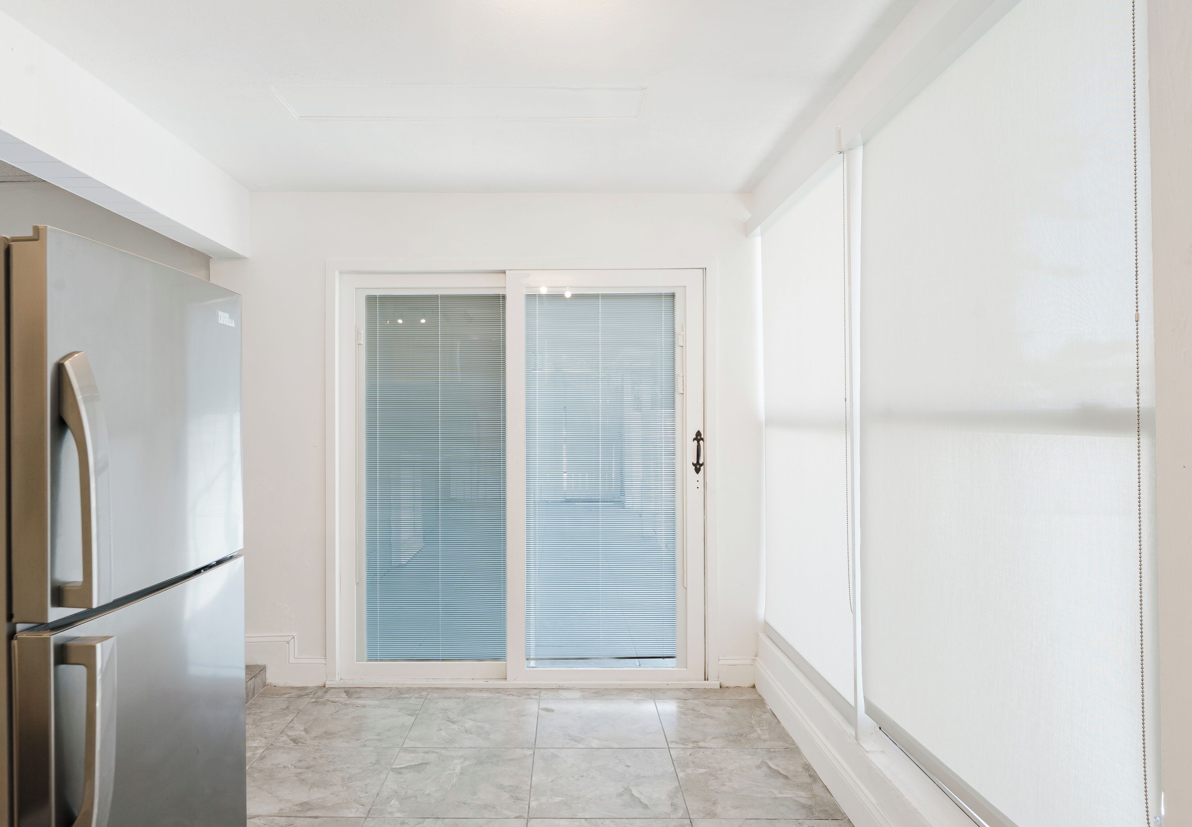Una cocina con refrigerador de acero inoxidable, una puerta corrediza de vidrio que da a un balcón y piso de baldosas.