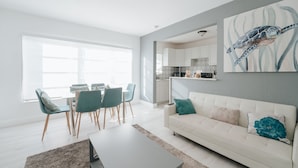 A modern living room with a dining area, a kitchen in the background, and a large window providing natural light. - PRAIA Hotel Hollywood (Hollywood)