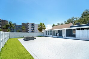 Un amplio patio exterior con cerca blanca, césped y un suelo de ladrillo.