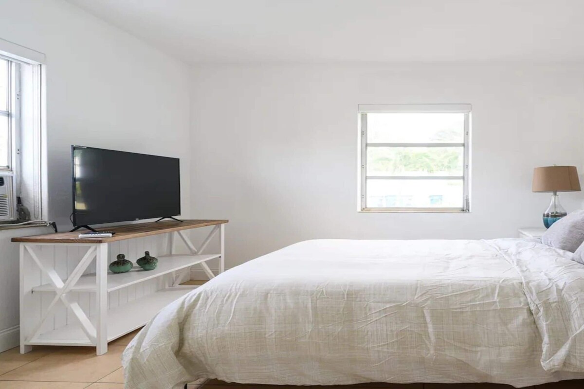 A bedroom with a bed, bedside lamps, a TV, and a window.