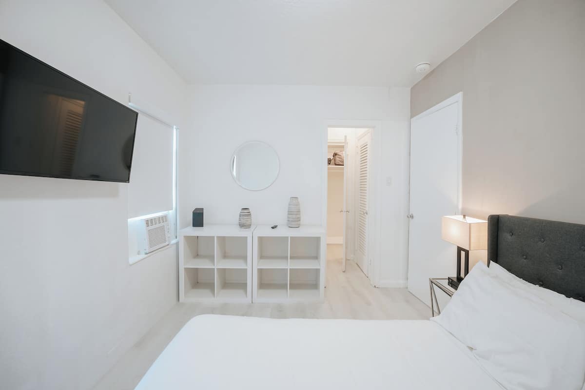 Une chambre à coucher comprenant un lit, un téléviseur fixé au mur, une table de chevet avec une lampe et une armoire.