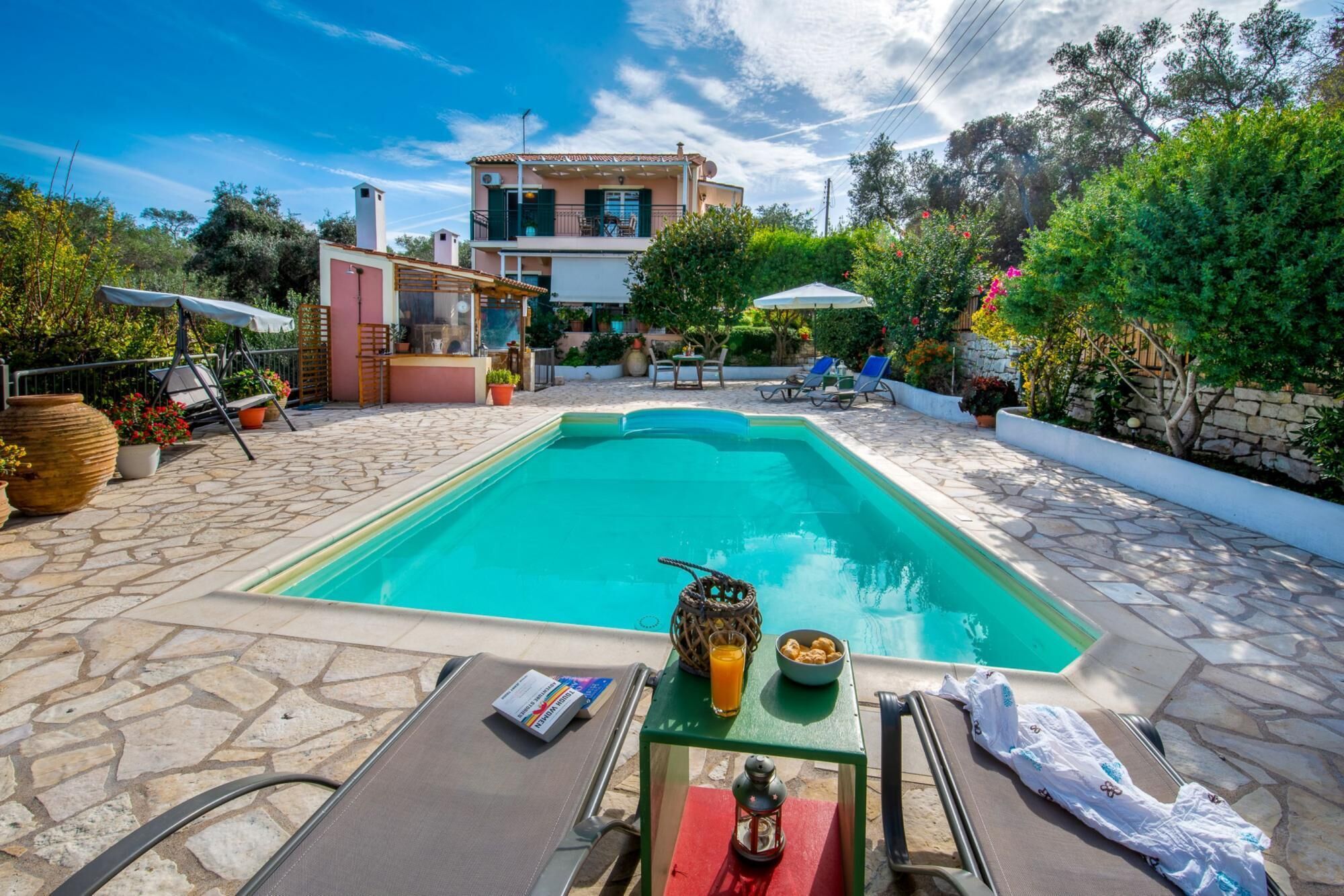 Ein Swimmingpool mit Liegestühlen, ein Tisch mit Flasche und Schale, und ein Gebäude im Hintergrund.