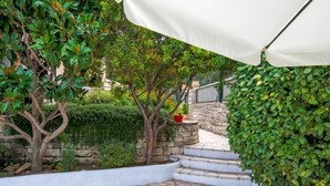 A stone-tiled patio with a white canopy, surrounded by lush greenery and a stone wall. - Villa Yiotta in Paxi (Paxos)