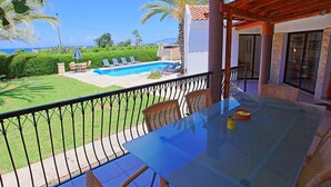 A balcony with a view of a swimming pool, outdoor furniture, and a clear sky. - Villa Maria Latchi in Latchi (Neo Chorio)